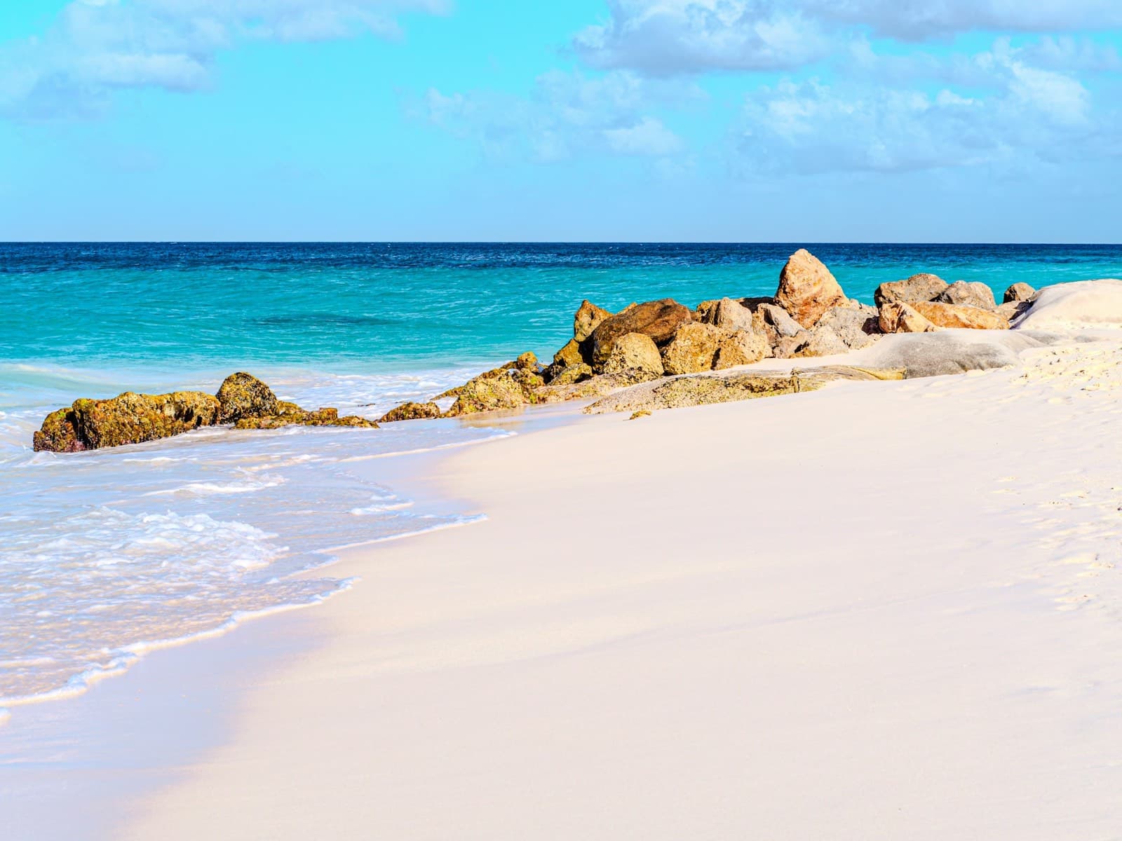 A quiet beach of soft white sand meeting clear turquoise water under a bright blue sky.