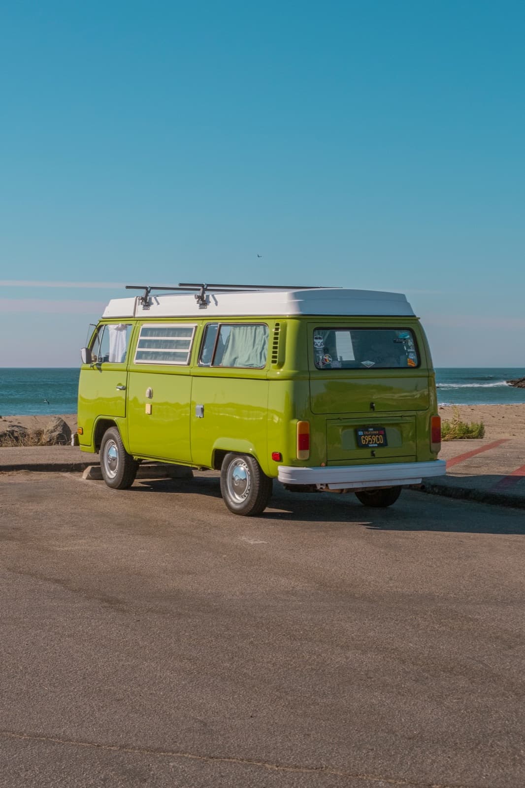 A green vintage camper van parked by the ocean under a clear sky.