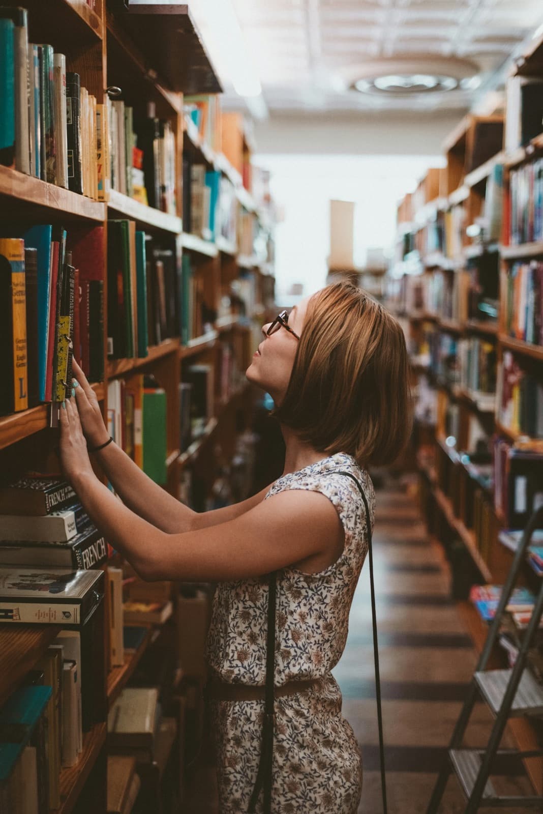 A woman choosing a book from tall library shelves.