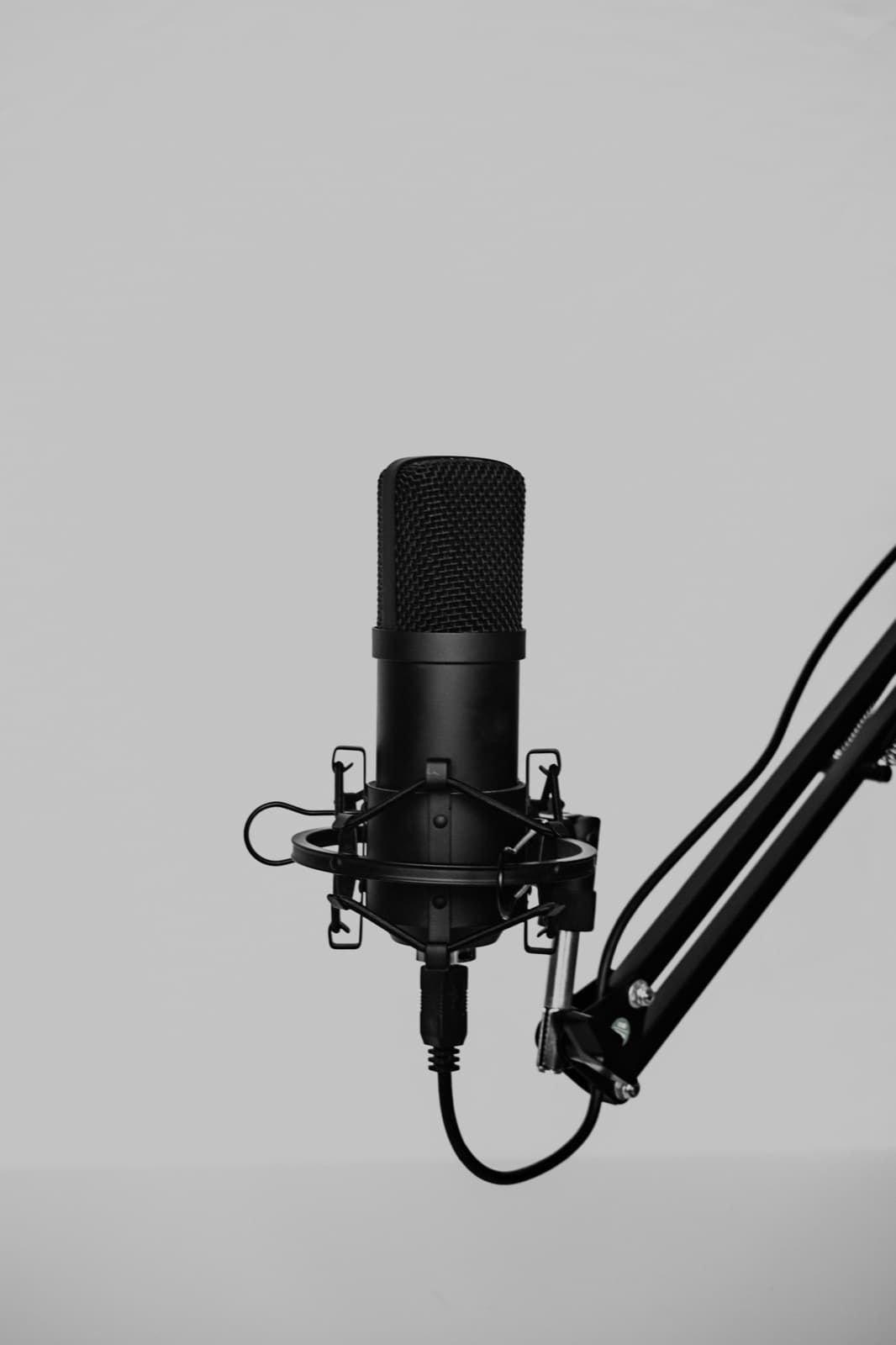 A black studio microphone on a boom arm against a plain grey wall.